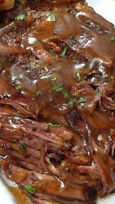 a white plate topped with roast beef covered in gravy and garnished with parsley