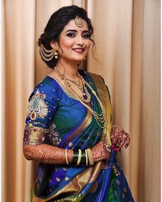 a woman in a blue and green sari with gold jewelry on her head, smiling at the camera