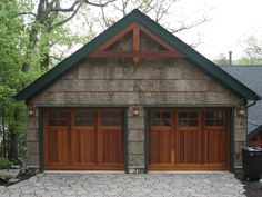 two garages with wooden doors and windows in front of a wooded area next to trees