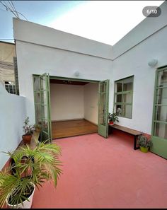 an empty courtyard with potted plants on the floor and green doors leading to another room