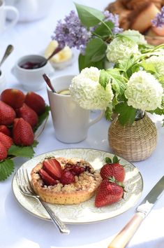 a table topped with plates and cups filled with desserts next to flowers on top of a white table cloth