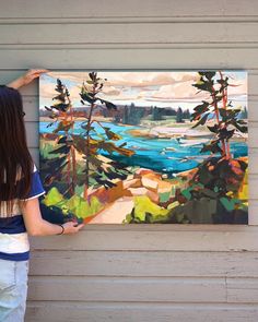 a woman holding up a painting on the side of a building next to a tree