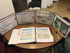 an open book sitting on top of a table next to two binders with papers