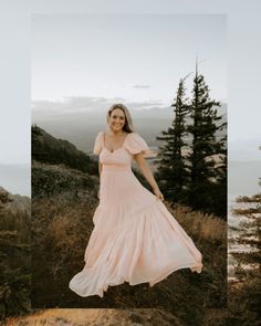 a woman in a long pink dress standing on top of a hill next to trees