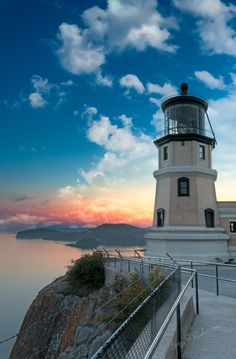 a lighthouse on top of a cliff overlooking the ocean at sunset with clouds in the sky