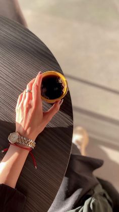 a woman holding a cup of coffee on top of a wooden table