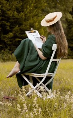 a woman in a green dress and hat sitting on a lawn chair reading a book