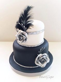 a three tiered cake with black and white frosting, feathers and roses on top