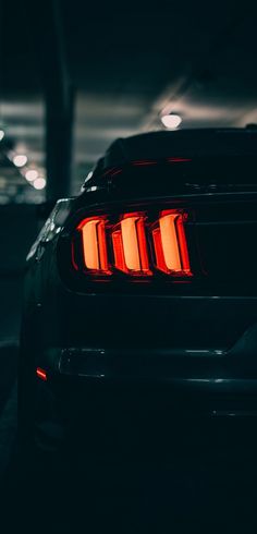 the rear end of a black mustang in a parking lot at night with its lights on