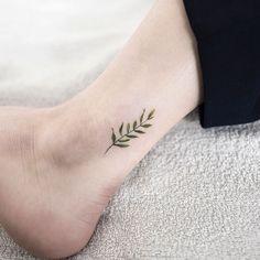 a woman's foot with a small green leaf tattoo on her left side ankle