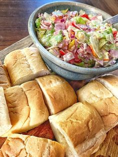 a wooden cutting board topped with sandwiches and a bowl of coleslaw