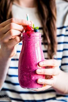 a woman holding a pink smoothie in her hand