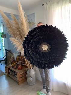 a man holding a large black flower in front of a white curtained room window