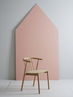 a wooden chair sitting in front of a pink wall next to a white and gray floor