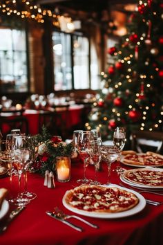 a table set with pizzas and silverware in front of a christmas tree