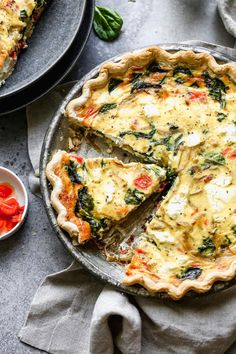 a quiche with cheese and spinach is on a plate next to a bowl of tomatoes