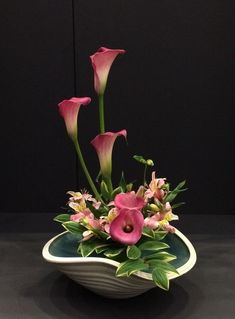 a bowl with flowers in it sitting on a black tableclothed surface next to a wall