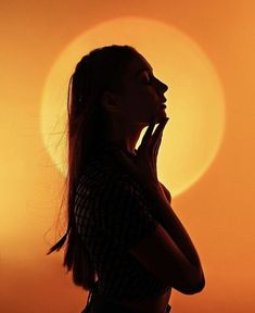 a woman standing in front of the sun with her hands to her face and looking up