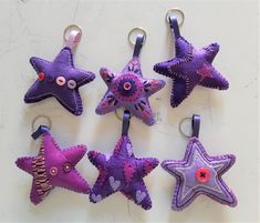 five purple and pink felt star ornaments hanging from hooks on a white surface with buttons