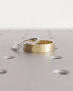 two wedding rings sitting on top of each other in the middle of a silver surface