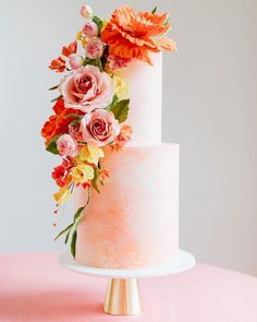 a three tiered white cake with flowers on the top and bottom, sitting on a pink table