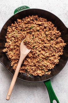 a skillet filled with ground meat and a wooden spoon on top of the skillet