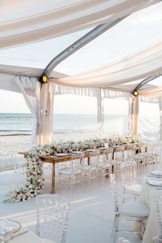 an outdoor wedding setup with white linens and flowers on the tables at the beach