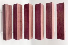 four pieces of wood are lined up in a row on a white wall, one is red and the other is pink