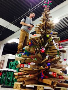 a man standing next to a christmas tree made out of cardboard boxes and other items