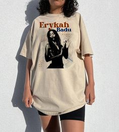 a woman standing in front of a white wall wearing a t - shirt with an image of erykah badu on it