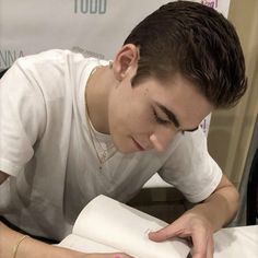 a young man laying on top of a bed next to an open book with writing on it