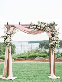 an outdoor wedding ceremony setup with pink and white flowers on the arch, greenery and water in the background