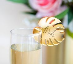 a close up of a wine glass and a gold bottle opener on a table with flowers in the background