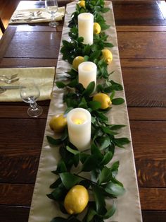 a long table with lemons and greenery on it, along with two candles