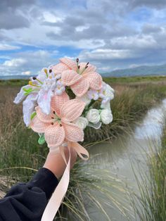 a hand holding a bouquet of flowers in front of a body of water on a cloudy day