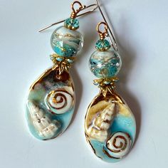 Blue long Shell earrings!  Gorgeous ceramic charms by the great artisan Annet Riabukhina paired with a beautiful artisan handmade lampwork rond bead. 22K gold lines are added by hand. The artist mark!  Swarovski faceted rondelles and gold tone and blue findings give a touch of sparkling and a rich look. All these chic and unique elements are suspended on gold filled hooks making these earrings allergy free. You're sure to attract admiration and everyone look with this fascinating unusual earrings. Very chic! Very ocean! Blue, aqua, beige, white  and gold in different textures and shapes give those earrings a special bohemian and romantic vibe.  They are about 2 3/4'' long from the top of ear wire. In all my photos, I am trying to depict colors as accurate as possible, but please be aware t Artisan Turquoise Earrings For Beach, Unique Blue Jewelry For Vacation, Handmade Blue Ocean-inspired Earrings, Artisan Czech Glass Jewelry For Beach, Unique Blue Earrings For Beach, Ceramic Charms, Earrings Ceramic, Blue Charm, Unusual Earrings