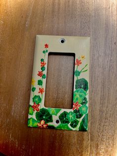 a light switch cover with flowers and leaves painted on the front, sitting on a wooden surface