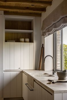 a kitchen with white cabinets and counter tops next to a window that looks out onto the trees outside