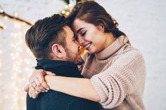 a man and woman embracing each other in front of a christmas tree with lights on it