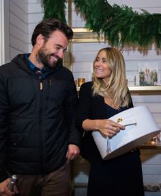 a man and woman standing next to each other in front of a christmas tree holding presents