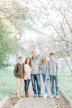 a family poses for a photo in front of some trees with pink blossoms on it