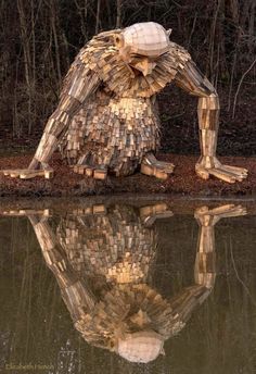 a sculpture made out of wood sticks sitting on top of a body of water with trees in the background