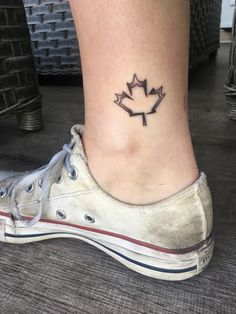 a woman's foot with a small maple leaf tattoo on the side of her ankle