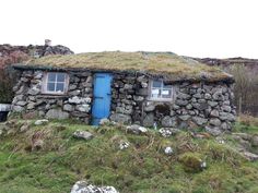 an old stone house with a grass roof and blue door in the middle of nowhere