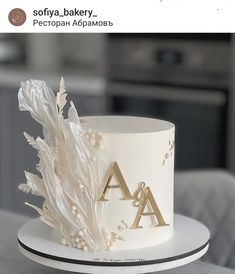 a white cake with gold letters and flowers on the top is sitting on a table