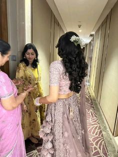 two women in sari are talking to each other on the hallway way with another woman standing next to them