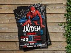 a spiderman birthday party card on a wooden table with greenery and leaves in the background