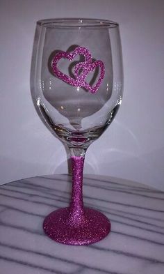 a wine glass with two hearts painted on the side and pink glitter in the middle