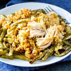 a white plate topped with green beans covered in chicken and stuffing next to a fork