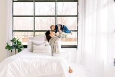 a woman laying on top of a white bed next to a window with lots of windows